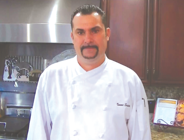 A man in white chef 's coat standing next to an oven.