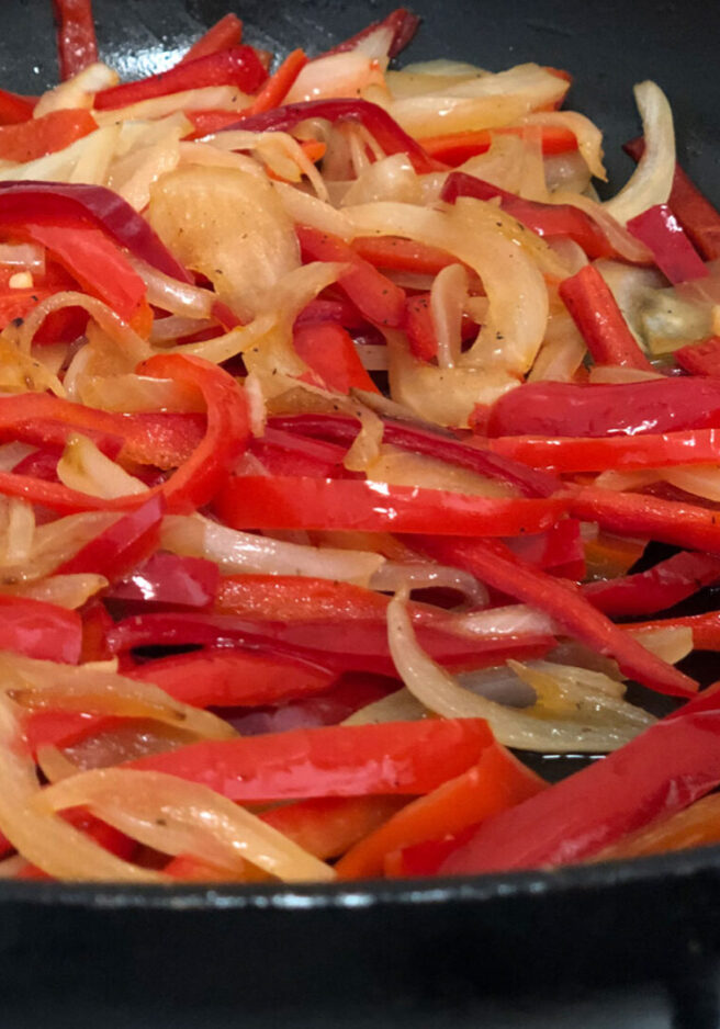 A pan of red peppers and onions in sauce.